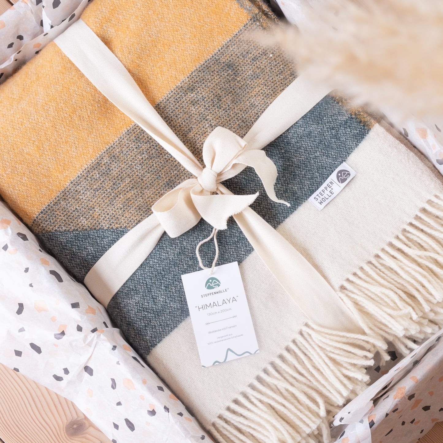 Die Wolldecke Himalaya liegt gefaltet und mit Schleife verziert im Versandkarton plastikfrei verpackt.