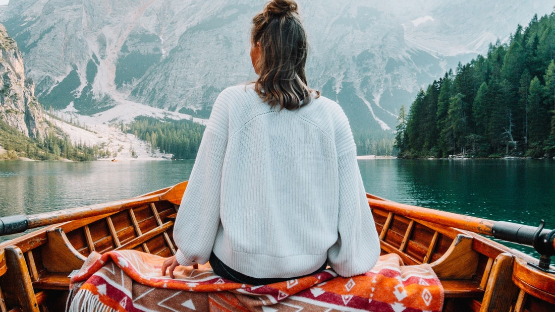Eine junge Frau sitzt auf einer gelben Wolldecke mit Ethno Muster am Fluss. 
