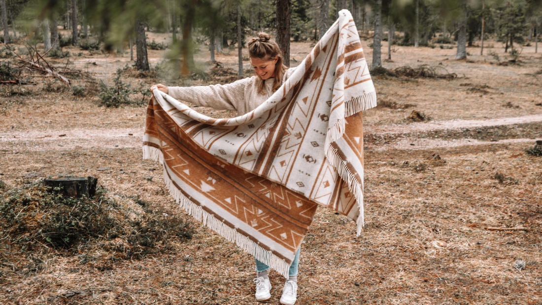 Eine junge Frau hält eine umweltfreundliche Picknickdecke aus Schurwolle in die Luft.