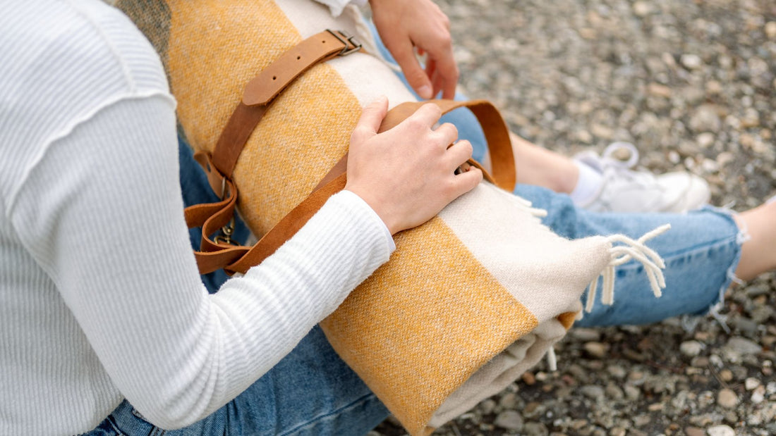 Eine Hand einer jungen Frau liegt auf einer zusammengerollten bunten Schurwolldecke. 