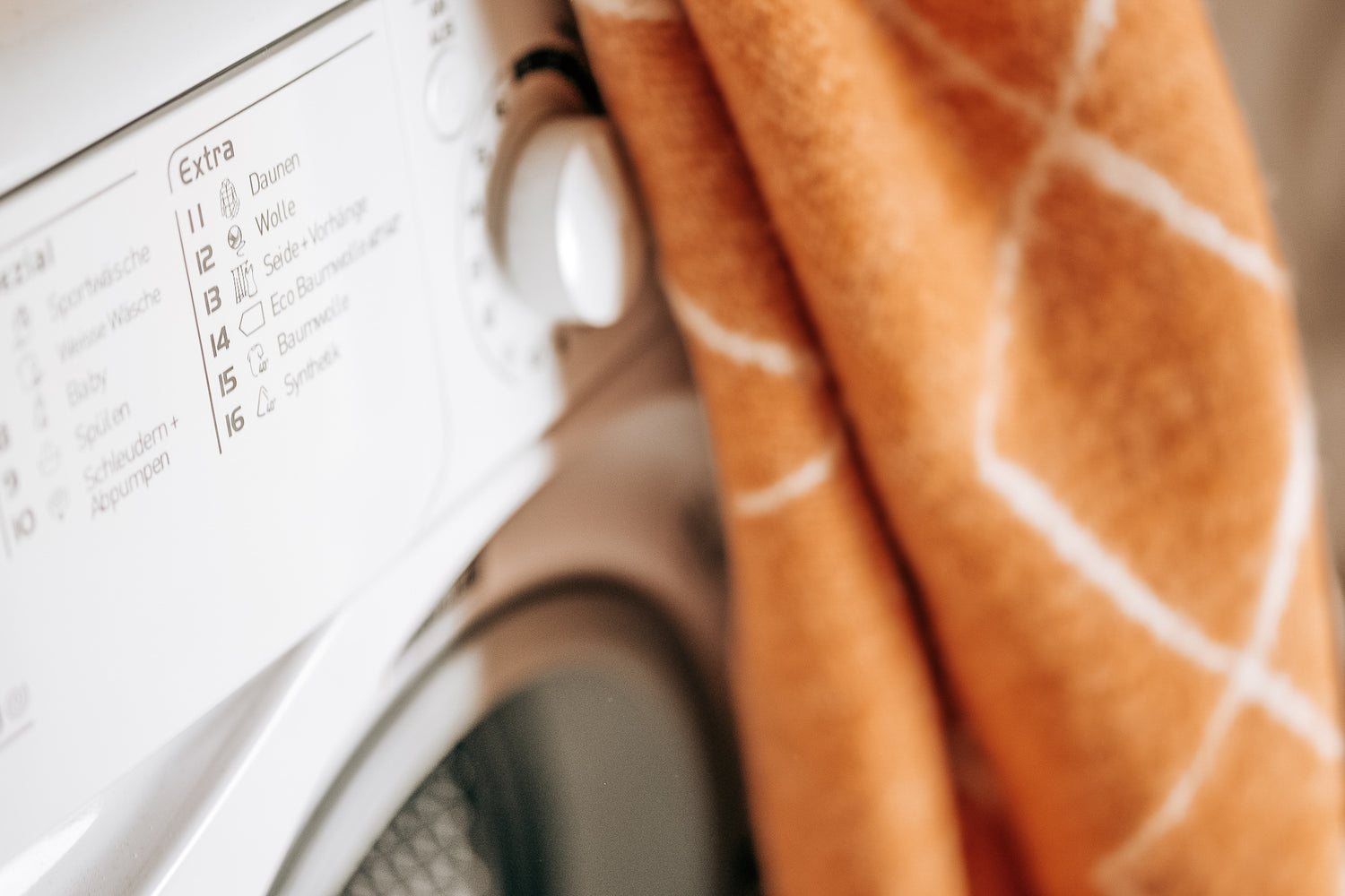 Eine gelbe Wolldecke liegt auf einer Waschmaschine zum Waschen bereit.
